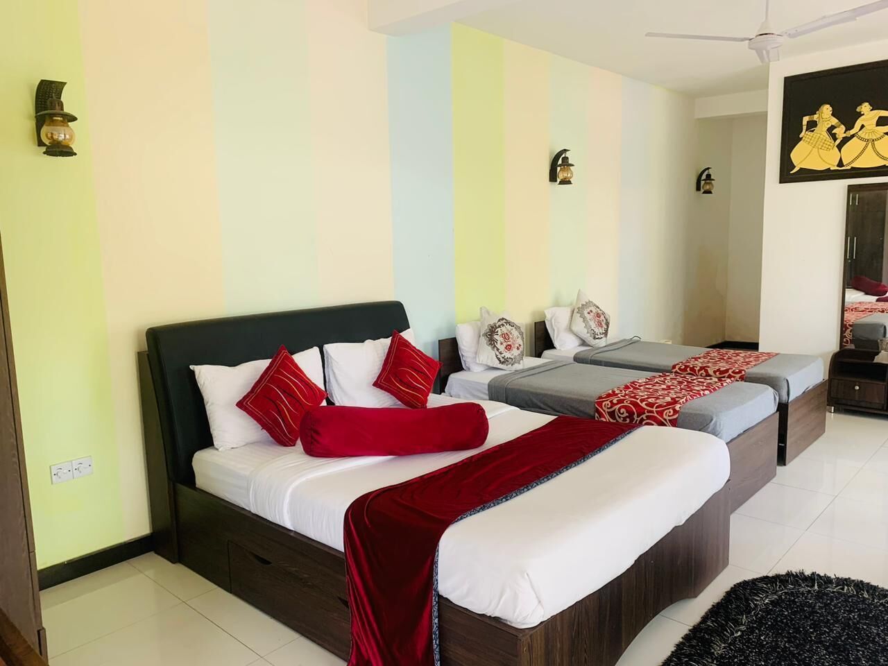 A hotel room with a large bed, two smaller beds, and a ceiling fan.