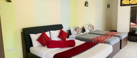 A hotel room with a large bed, two smaller beds, and a ceiling fan.