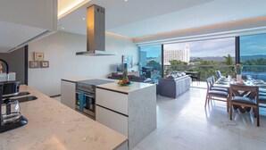 A modern kitchen with a central island, a dining area with a view, and a large window overlooking a cityscape. - NEW Beachfront Marítima Condos 2 Pools (Nuevo Nayarit)