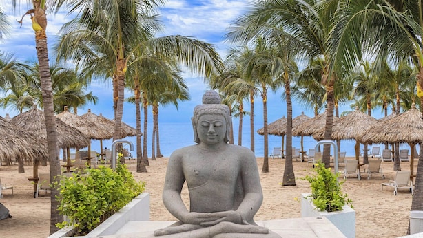 A Buddha statue on a beach with palm trees and thatched umbrellas. - NEW Beachfront Marítima Condos 2 Pools (Nuevo Nayarit)