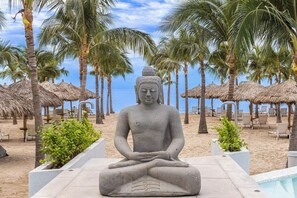 A Buddha statue on a beach with palm trees and thatched umbrellas. - NEW Beachfront Marítima Condos 2 Pools (Nuevo Nayarit)