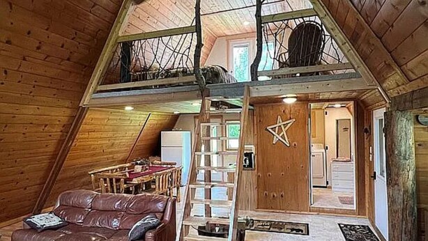 Un acogedor espacio tipo loft con techo de madera, un sofá de cuero marrón, una escalera y una puerta en forma de estrella.