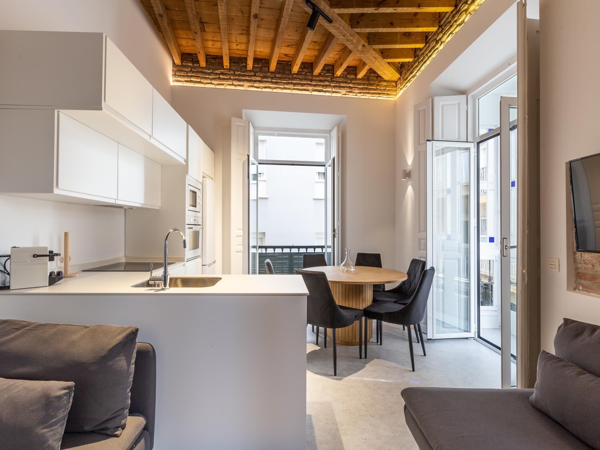 Una cocina moderna con armarios blancos, techo de madera y un comedor con mesa redonda y sillas negras.