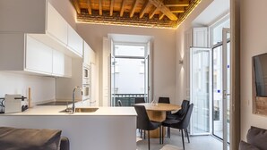 Eine moderne Küche mit weißen Schränken, einer Holzbalkendecke und einem Essbereich mit rundem Tisch und schwarzen Stühlen.
