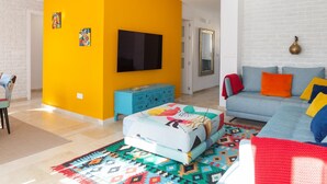 A bright living room with a yellow accent wall, a sofa with colorful cushions, a television, and a blue cabinet. - Central and bright apartment with balconies (Málaga)