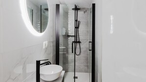 Une salle de bain moderne avec un lavabo blanc, un grand miroir et une douche séparée par des parois en verre.