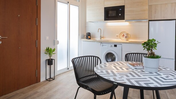 Une cuisine moderne équipée d’un four à micro-ondes, d’un évier et d’un lave-linge. On y trouve également un coin repas avec une table et des chaises, ainsi qu’une porte en bois.