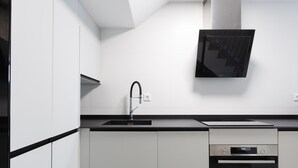 A modern kitchen with white cabinets, a black countertop, a stainless steel sink, a built-in oven, and a wall-mounted TV. - Nice apartment in the Central District (Málaga)