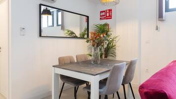 Un comedor con una mesa blanca, sillas grises, un jarrón con flores y una lámpara colgante.