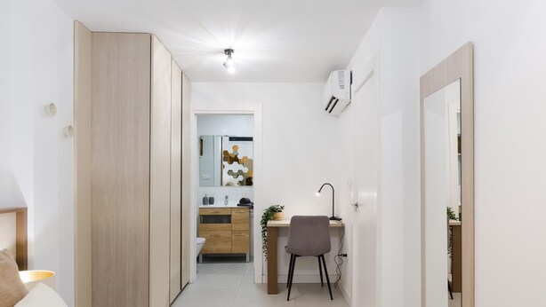 A modern bedroom with a bed, a desk with a chair, a wardrobe, and a bathroom visible through an open door. - Nice apartment in the Central District (Málaga)