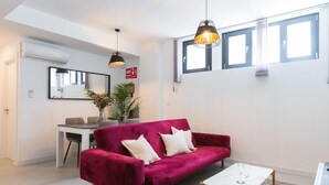 A modern living room with a red velvet sofa, a white coffee table, and a dining area with a white table and chairs. - Nice apartment in the Central District (Málaga)
