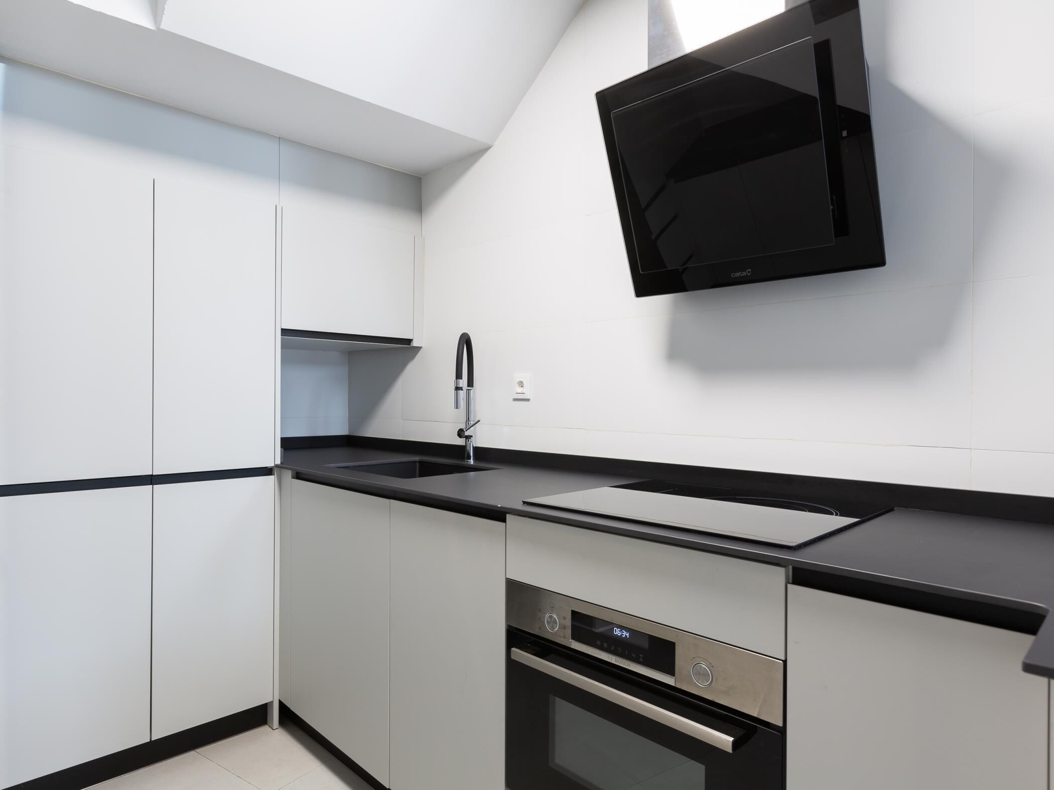 Una cocina moderna con armarios blancos, encimera negra, horno empotrado y televisor montado en la pared.