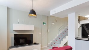 A modern living room with a flat-screen TV, a white entertainment unit, a red sofa, and a staircase leading to the upper floor. - Nice apartment in the Central District (Málaga)