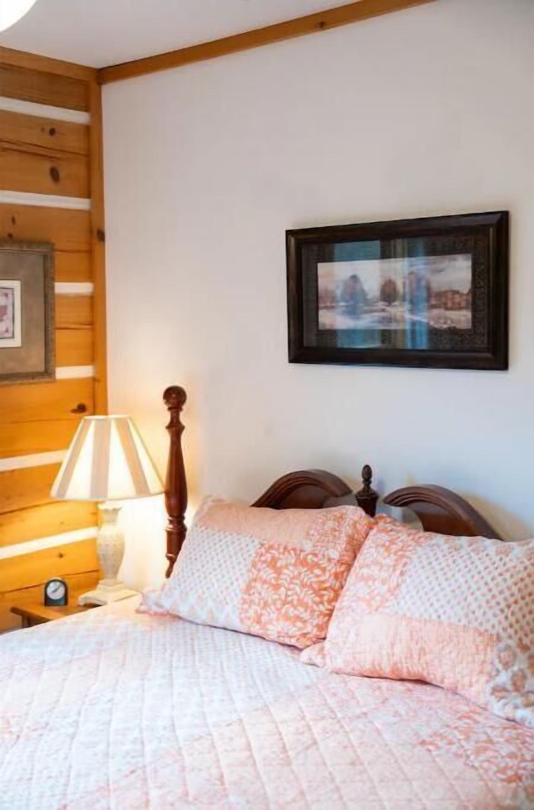 Ein Schlafzimmer mit einem Holzkopfteil, einem Bett mit gemusterten Bettbezügen, einem Nachttisch mit Lampe und einem gerahmten Bild an der Wand.