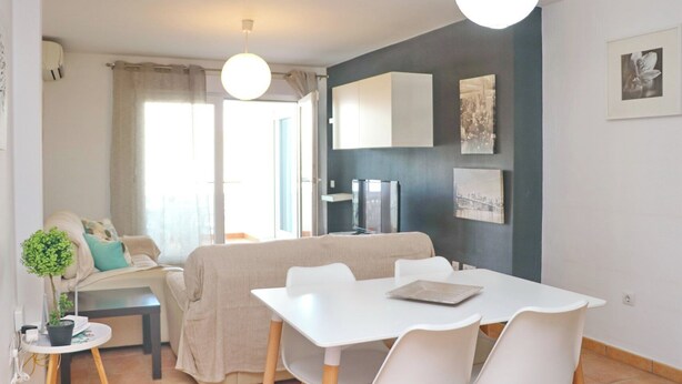 A modern living room with a sofa, a dining table with chairs, a TV, and artwork on the wall. - Apartamento Bateles Cerca de la Playa (Conil de la Fra.)