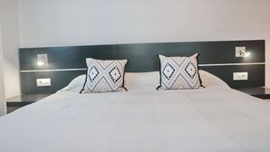 A large bed with a white bedspread and two decorative pillows with a geometric pattern. - Apartamento Bateles Cerca de la Playa (Conil de la Fra.)