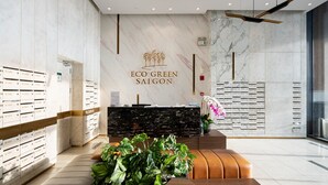 A modern reception area with a marble wall, a reception desk, and a plant. - Eco Green Apartment- Minimalist Home (Ho Chi Minh City)