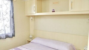 A bedroom with a bed, a nightstand, a wall-mounted cabinet, and a window with a curtain. - Bungalow Puntalejo in Conil (Conil de la Frontera)