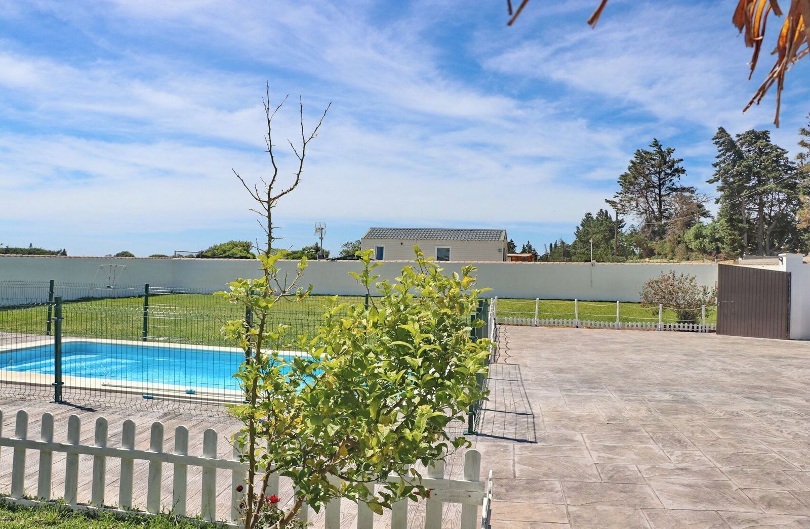 A swimming pool with a fence, a white picket fence, and a view of a building in the background.