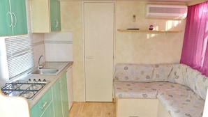 A compact kitchen with a gas stove, sink, and a small refrigerator. There is a built-in bench with a patterned cushion. - Bungalow Puntalejo in Conil (Conil de la Frontera)
