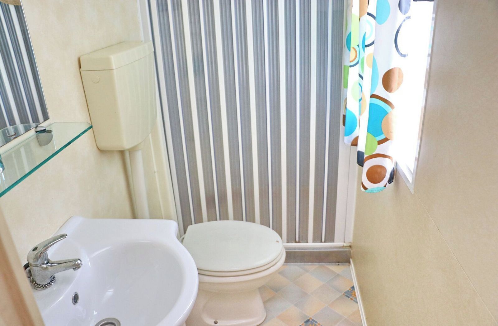 A small bathroom with a white sink, toilet, and a glass shower enclosure.