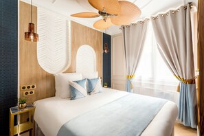 Une chambre d’hôtel moderne avec un grand lit, un ventilateur de plafond et une vue sur la ville.