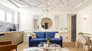 A modern living room with a blue sofa, a glass coffee table, and a chandelier. - Merveil - Luxury Suite - Notre Dame - Boulangers (Paris)