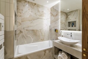 Ein modernes Badezimmer mit Marmorwand, einer freistehenden Badewanne, einem Waschbecken mit Ablagefläche und einem Holzschrank.