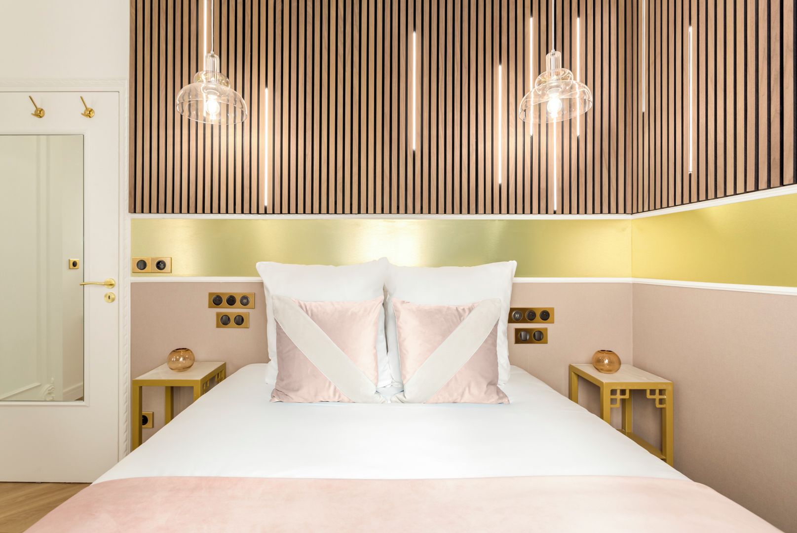 Un dormitorio moderno con una cama grande, dos mesitas de noche, un cabecero de listones de madera y luces colgantes.