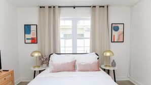 Een slaapkamer met een bed, twee nachtkastjes met lampen, een kaptafel en twee abstracte schilderijen aan de muur.