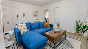 Een moderne woonkamer met een blauwe hoekbank, een houten salontafel en een gestreept vloerkleed.