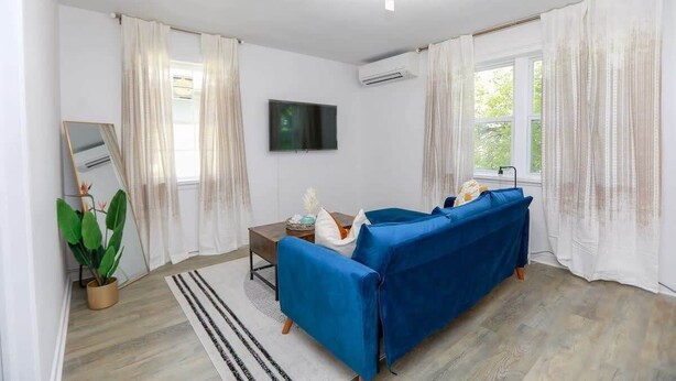 A living room with a blue sofa, a flat-screen TV, and a potted plant. - Anchor Breeze | Sojourn | Steps to the Beach (Norfolk)