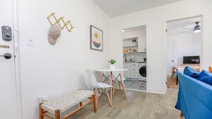 A modern, well-lit room with a dining area, a bench, a small table with chairs, and a kitchen in the background. - Anchor Breeze | Sojourn | Steps to the Beach (Norfolk)