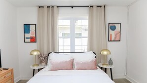 A bedroom with a bed, two bedside tables with lamps, a dresser, and two abstract paintings on the walls. - Anchor Breeze | Sojourn | Steps to the Beach (Norfolk)
