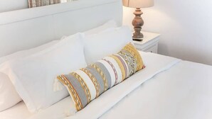 A neatly made bed with white linens and a multicolored striped pillow. - Sojourn | Hideaway Bay | 2 BR (Norfolk)
