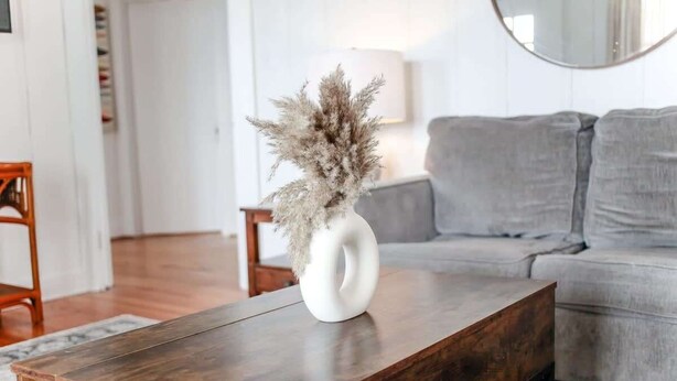 A modern living room with a wooden coffee table, a white vase with dried plants, and a grey sofa. - Sojourn | Hideaway Bay | 2 BR (Norfolk)