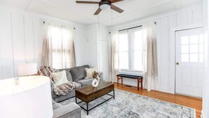 A spacious living room with a grey sofa, a wooden coffee table, and a large window with curtains. - Sojourn | Hideaway Bay | 2 BR (Norfolk)