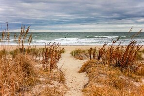 A sandy beach path leading to the ocean with overcast skies.