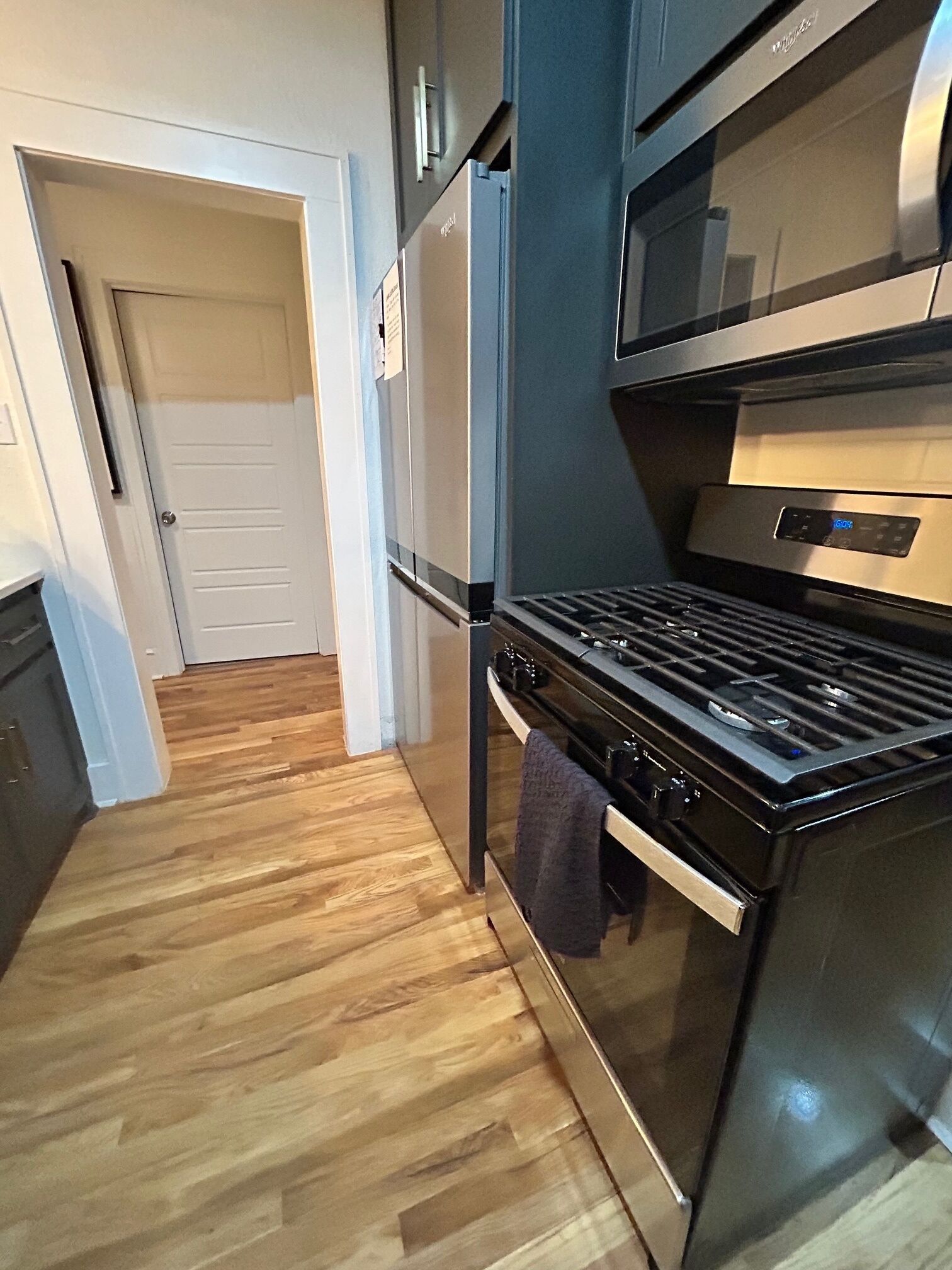 A kitchen with a stainless steel stove, a refrigerator, and wooden flooring.