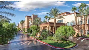 A hotel with a central courtyard, palm trees, and a curved driveway. - Perfect Super Bowl Week Condo - 10 minutes from stadium (Las Vegas)