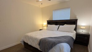 Un dormitorio con cama, dos mesitas de noche, ventilador de techo y ventana con persianas.
