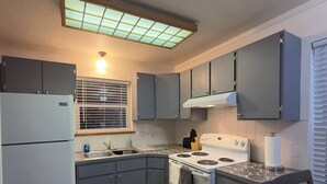 Una cocina compacta con armarios grises, una estufa blanca y una ventana con persianas.