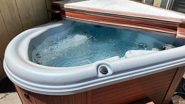 Un jacuzzi con revestimiento de madera y el interior blanco, cubierto parcialmente por una tapa de madera.