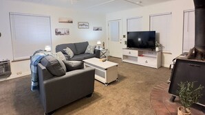 Una sala de estar moderna con un sofá gris, una mesa de centro blanca y un televisor de pantalla plana sobre un mueble blanco.