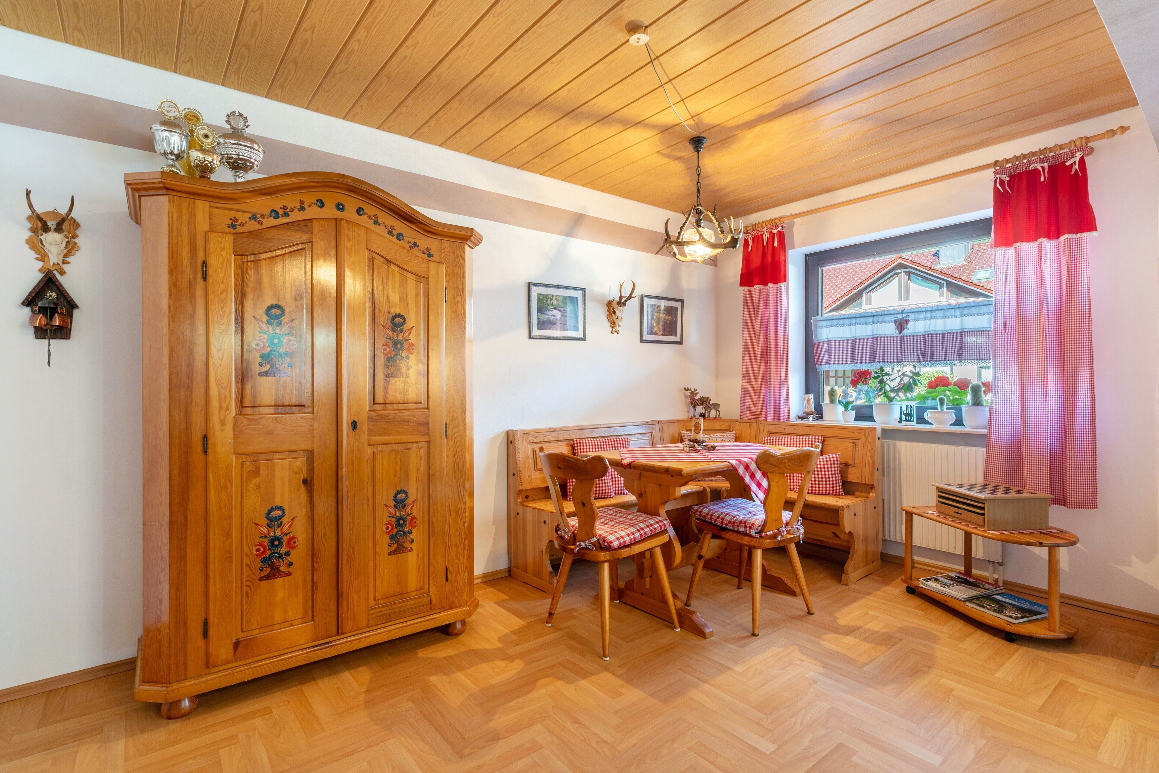Una mesa de comedor de madera con sillas, un armario de madera y un ventanal con cortinas rojas.