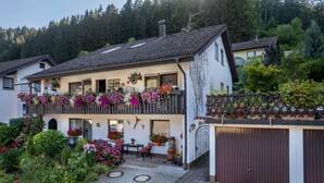 Ein zweigeschossiges Haus mit Balkon, Garage und Garten mit verschiedenen Pflanzen und Blumen.