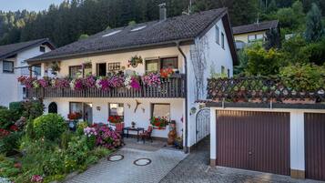 Ein zweigeschossiges Haus mit Balkon, Garage und Garten mit verschiedenen Pflanzen und Blumen.