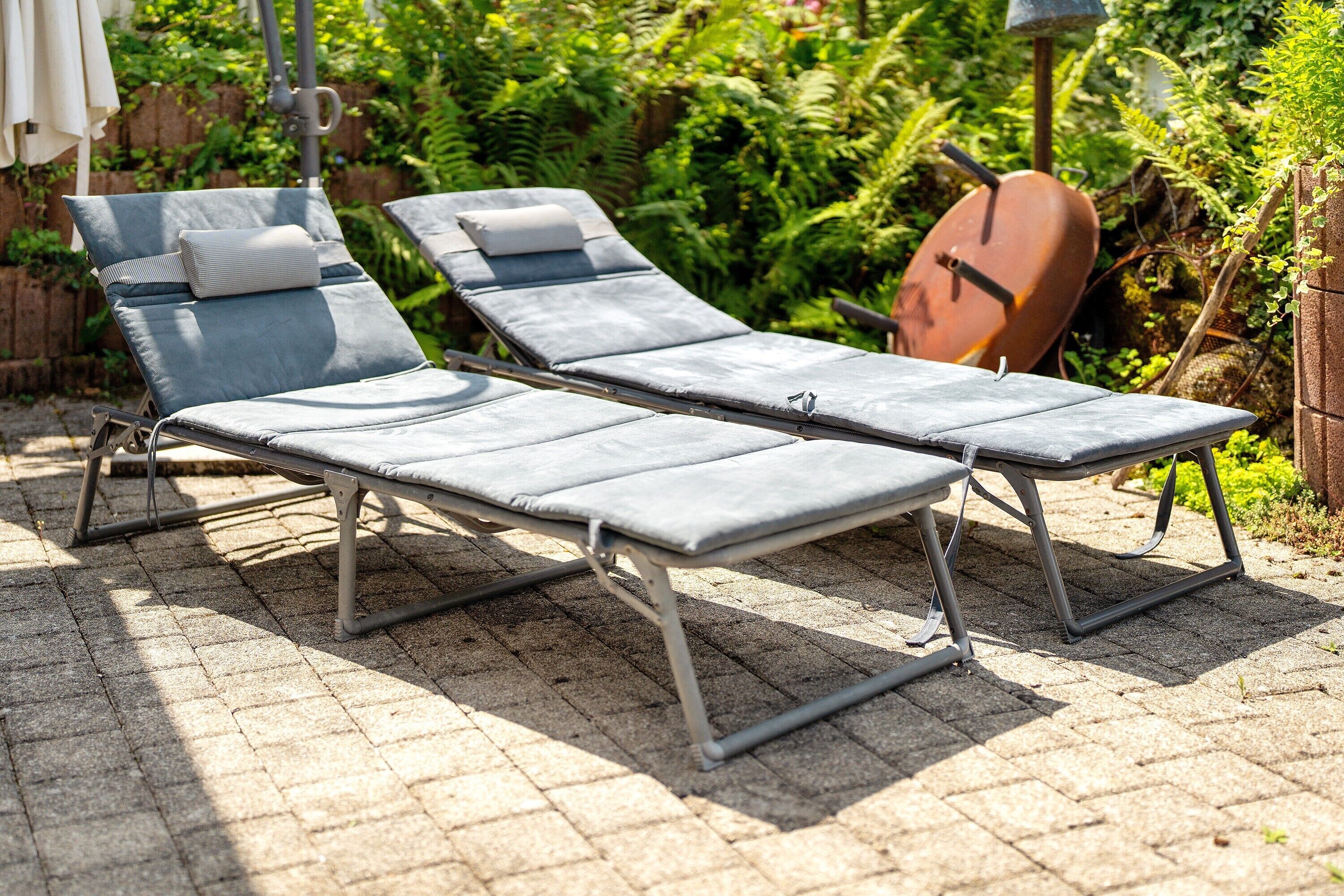 Two sun loungers with cushions, a metal frame, and a brick patio.