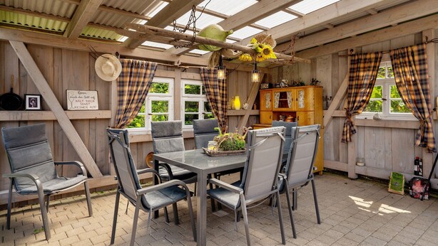 Un intérieur en bois avec une table et des chaises, un luminaire suspendu et des rideaux à carreaux.