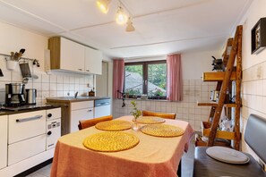 A kitchen with white cabinets, a dining table with yellow placemats, a wooden ladder shelf, and a window with pink curtains.